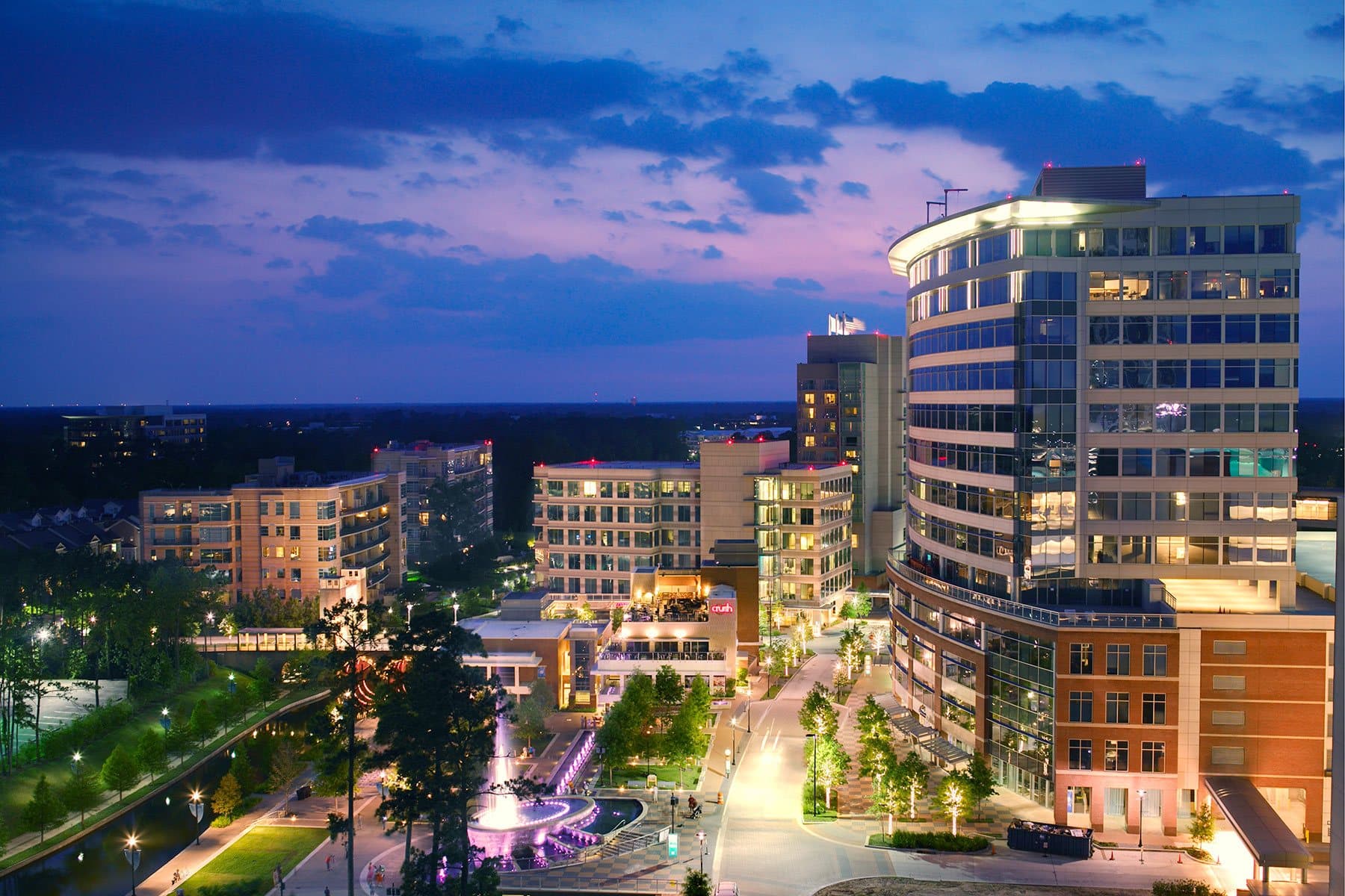 The office tower at 24 Waterway Avenue in The Woodlands at dusk, its windows lit against a blue evening sky