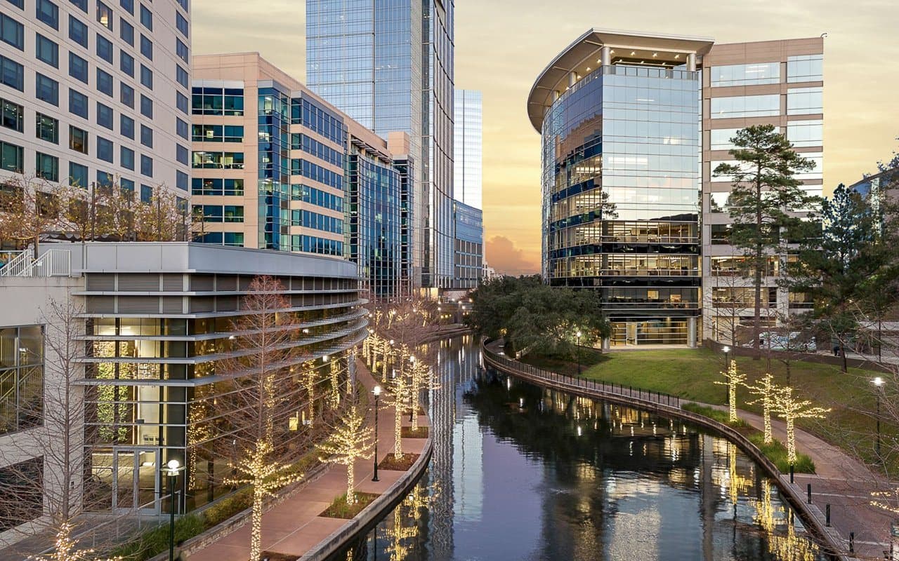 The Woodlands Waterway at dusk, lined with office towers and trees strung with lights